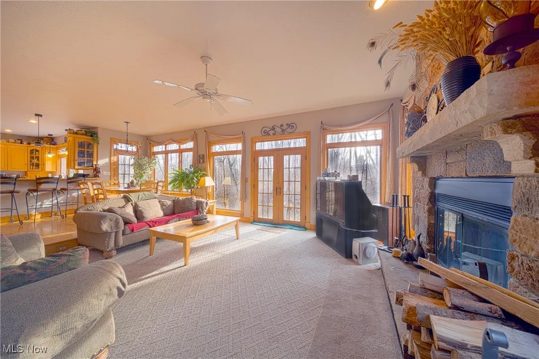 Living room featuring a stone fireplace, plenty of natural light, ceiling fan, and french doors
