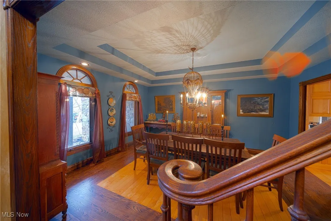 Dining area featuring light hardwood / wood-style flooring, a raised ceiling, a textured ceiling, and a notable chandelier