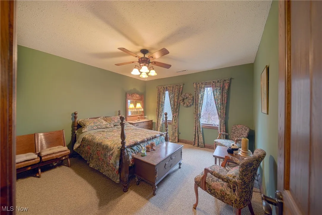 Bedroom with light colored carpet, ceiling fan, and a textured ceiling