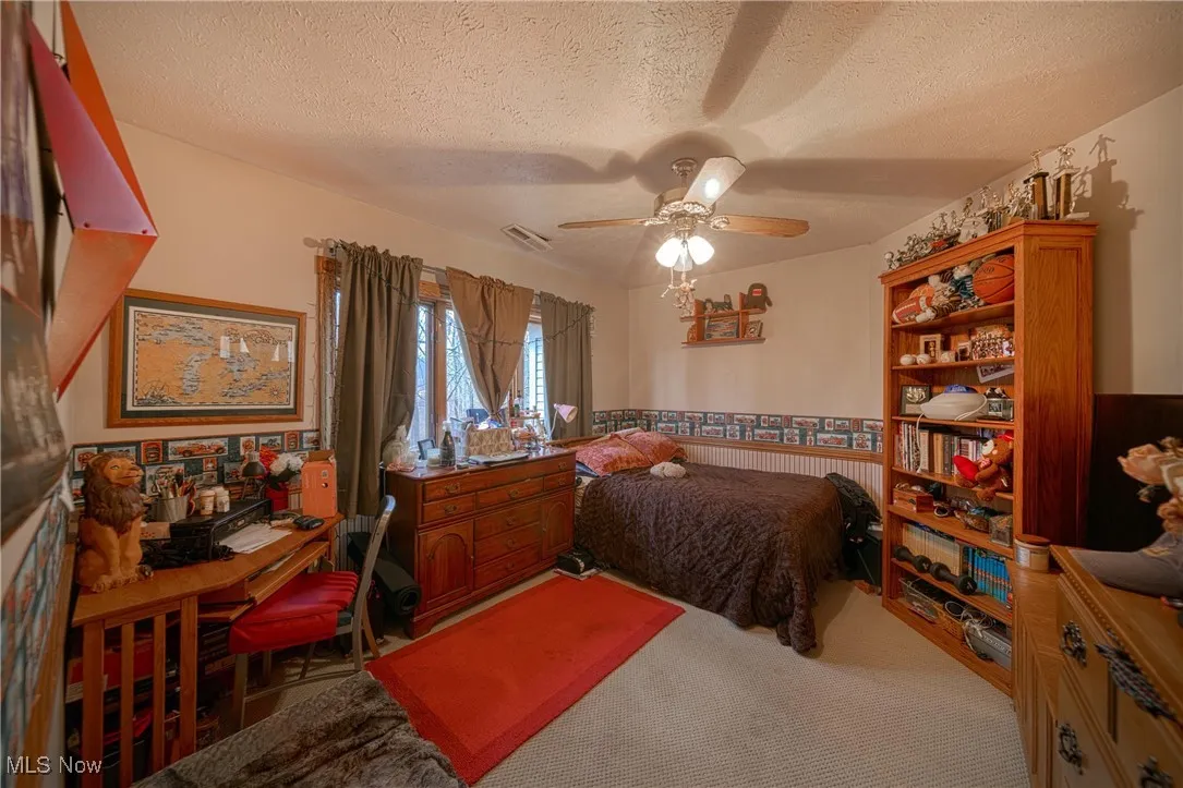 Carpeted bedroom featuring ceiling fan and a textured ceiling