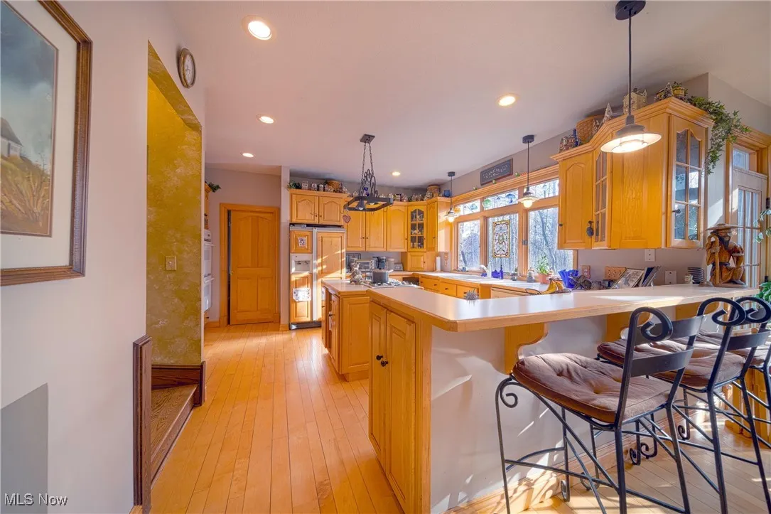 Kitchen with light hardwood / wood-style floors, paneled refrigerator, a breakfast bar, pendant lighting, and kitchen peninsula