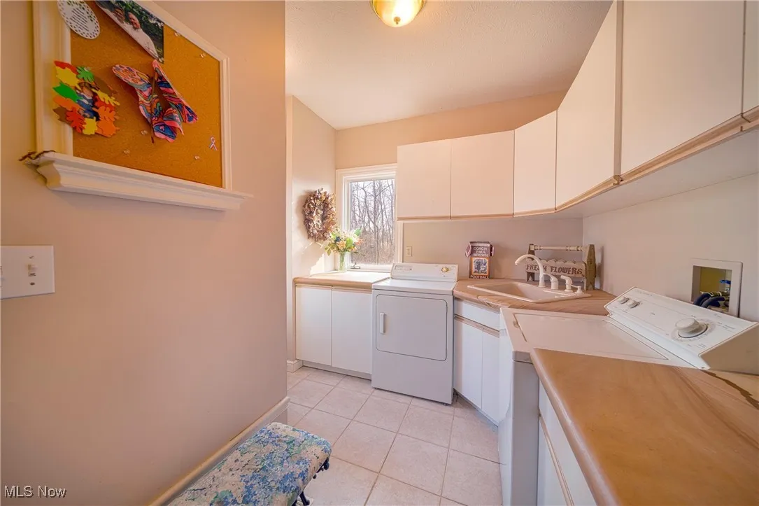 Washroom with washer hookup, washer and clothes dryer, cabinets, sink, and light tile floors