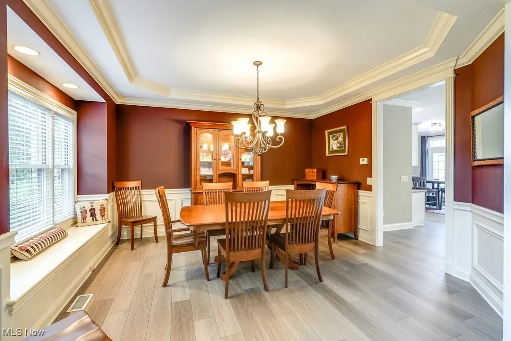 Dining space with light hardwood / wood-style flooring, a chandelier, a raised ceiling, and crown molding