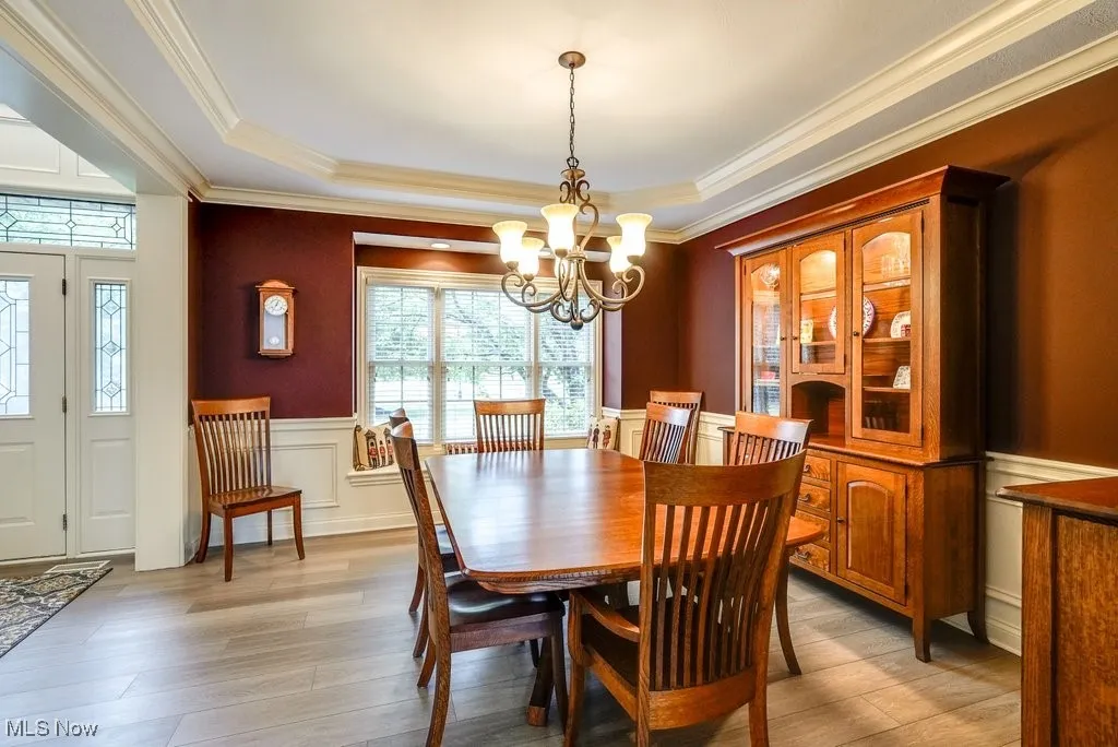 Dining space featuring light hardwood / wood-style floors, ornamental molding, a tray ceiling, and a notable chandelier