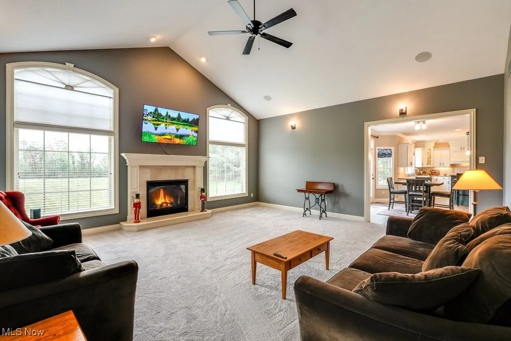 Carpeted living room with high vaulted ceiling, a tiled fireplace, ceiling fan, and plenty of natural light