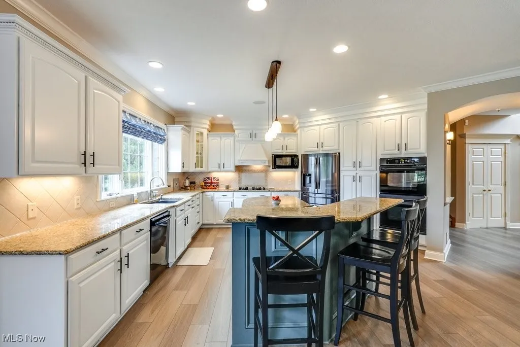 Kitchen with white cabinets, light wood-type flooring, a center island, and black appliances