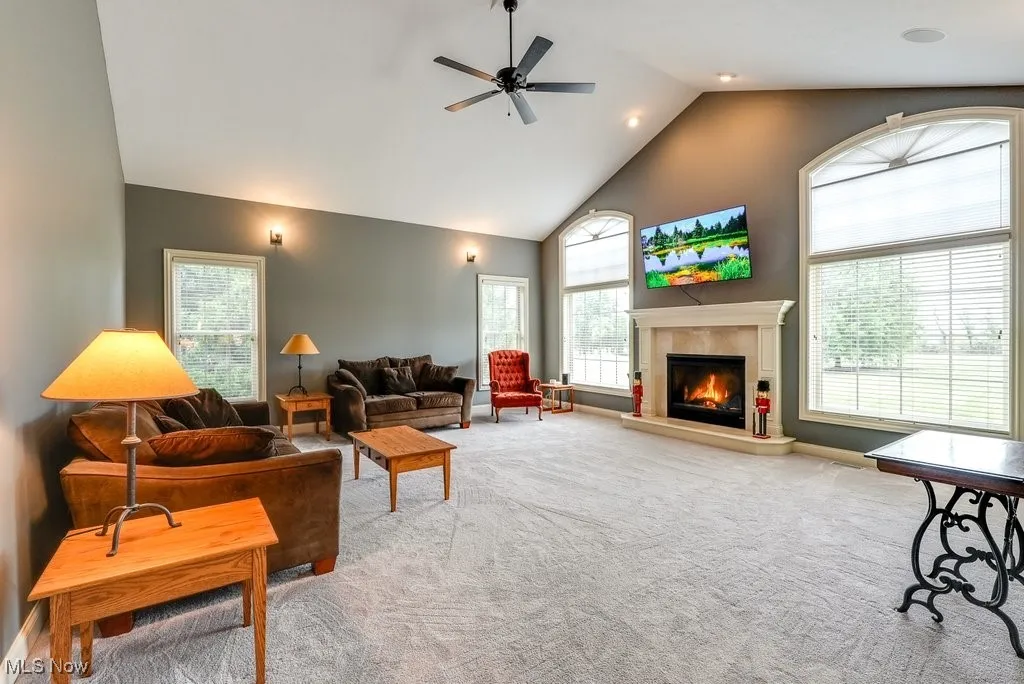 Carpeted living room with ceiling fan, high vaulted ceiling, and a tile fireplace