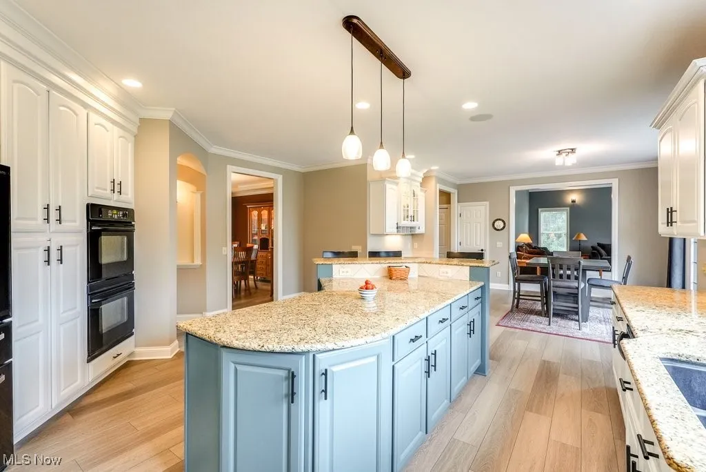 Kitchen with blue cabinets, light wood-type flooring, hanging light fixtures, and white cabinetry