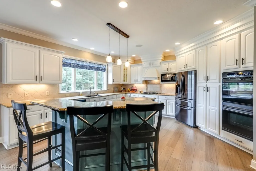 Kitchen with custom range hood, light stone counters, white cabinets, a breakfast bar area, and black appliances