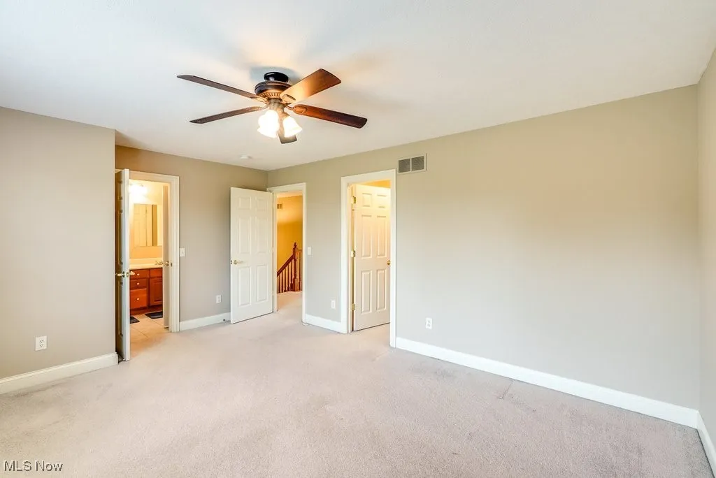 Unfurnished bedroom featuring ceiling fan, light colored carpet, and ensuite bathroom