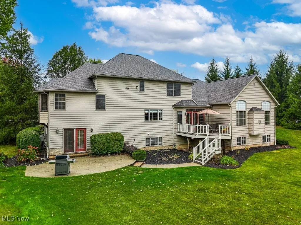 Back of property with a wooden deck, a patio, and a yard