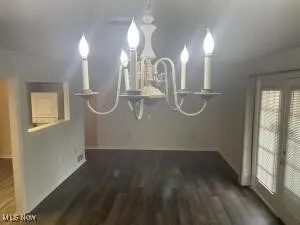 Unfurnished dining area featuring vaulted ceiling, a notable chandelier, and dark wood-type flooring