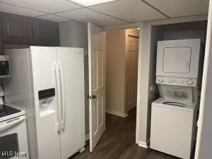 Kitchen with white appliances, stacked washer / drying machine, dark wood-type flooring, and a paneled ceiling