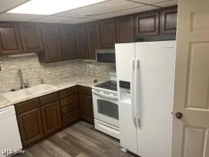 Kitchen with dark brown cabinetry, sink, white appliances, wood-type flooring, and decorative backsplash