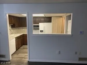 Kitchen featuring white appliances, hardwood / wood-style flooring, dark brown cabinetry, and tasteful backsplash