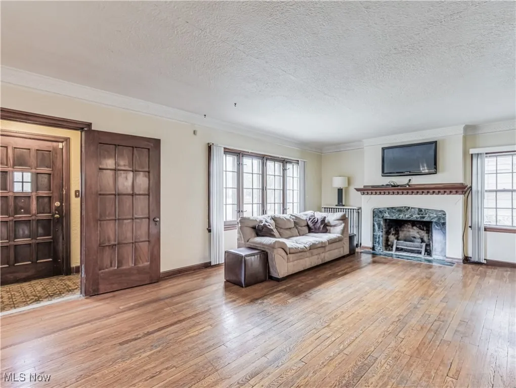 Living room featuring light hardwood wood-style flooring, a wood burning fireplace, a textured ceiling, and crown molding