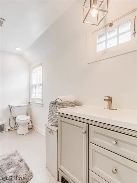 Bathroom with tile patterned flooring, lofted ceiling, vanity, and toilet