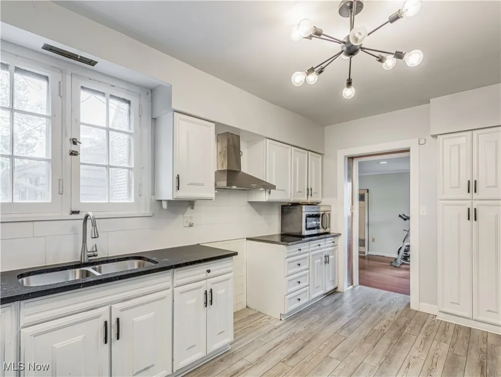 Updated kitchen featuring light wood-type flooring, white cabinetry, range hood, and backsplash