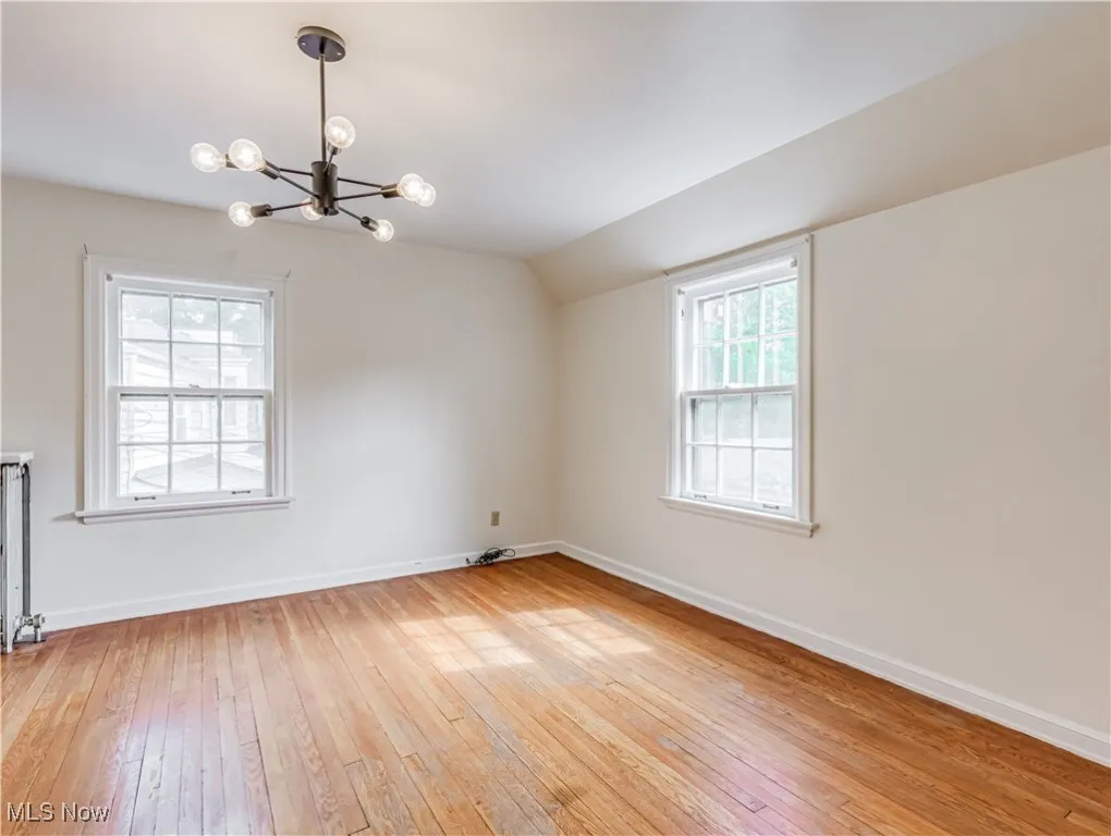 Spare room featuring a notable chandelier, vaulted ceiling, hardwood / wood-style flooring, and a wealth of natural light