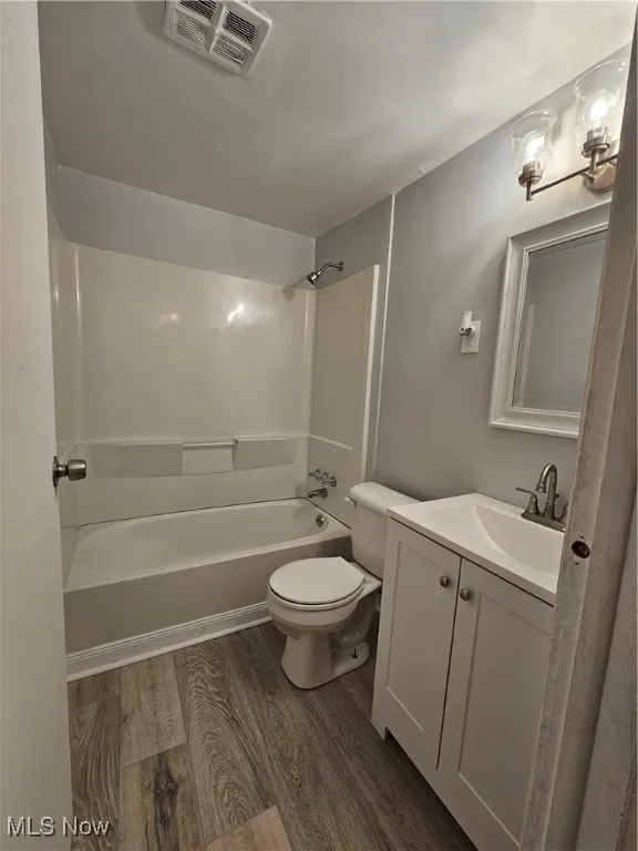 Full bathroom with bathing tub / shower combination, toilet, vanity, and hardwood / wood-style floors