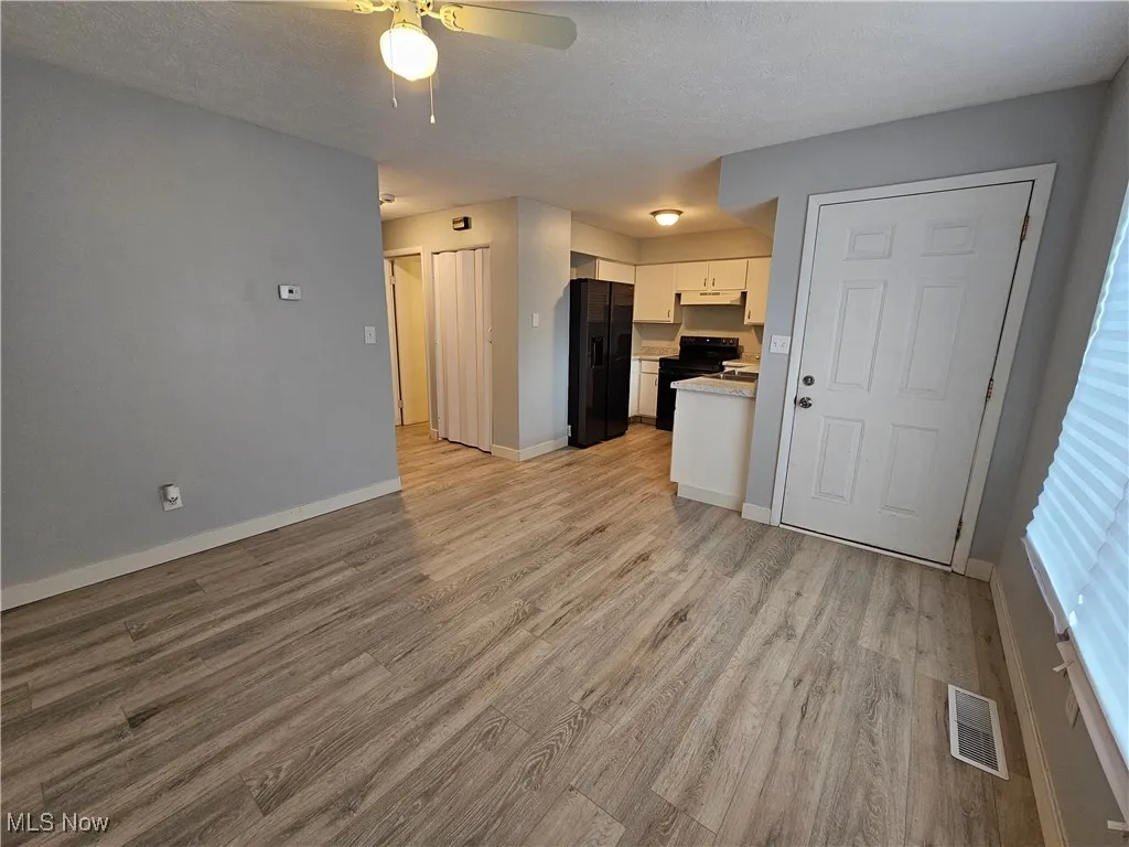 Unfurnished living room featuring light wood-type flooring, a textured ceiling, and ceiling fan