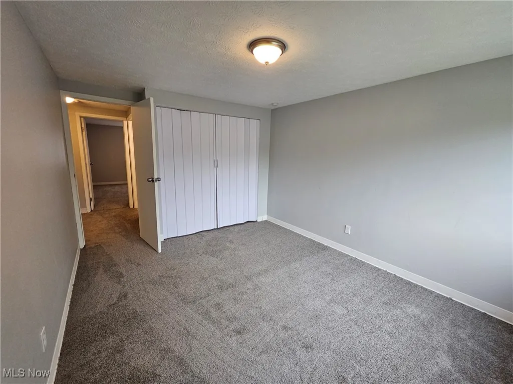 Unfurnished bedroom featuring a textured ceiling, a closet, and dark colored carpet