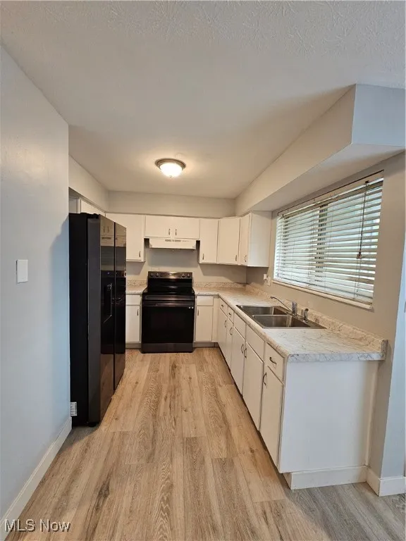 Kitchen with fridge, white cabinetry, stove, and light hardwood / wood-style floors