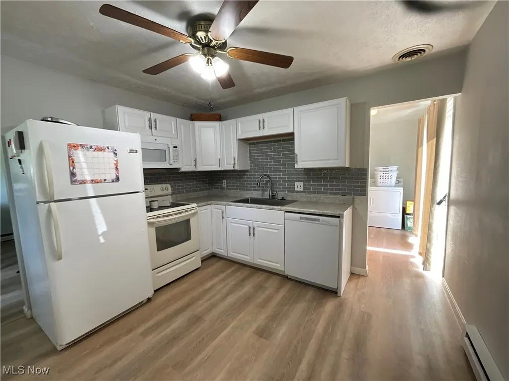 Kitchen with sink, white cabinetry, a baseboard radiator, white appliances, and washer / clothes dryer