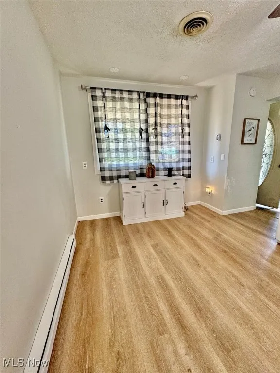 Empty room with a baseboard heating unit, a textured ceiling, and light wood-type flooring