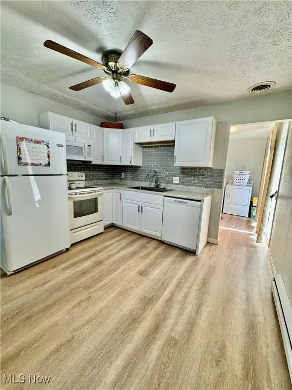 Kitchen with sink, white cabinetry, baseboard heating, white appliances, and backsplash