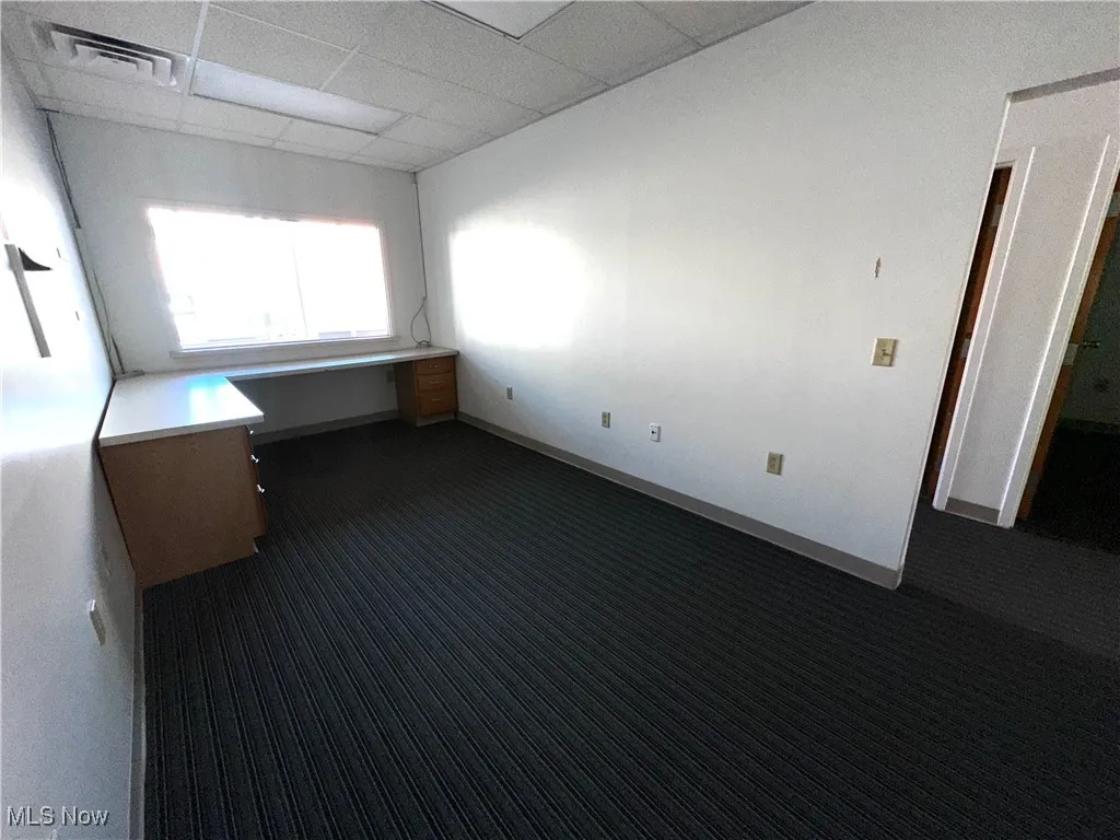 Spare room featuring dark carpet, a paneled ceiling, and built in desk