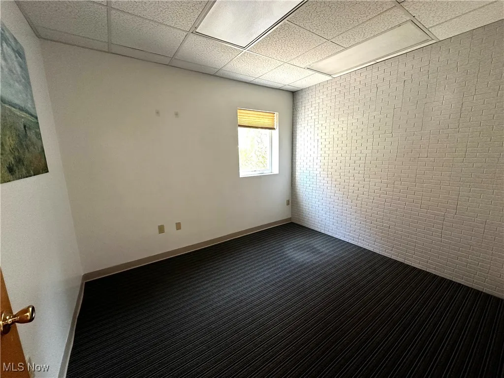 Spare room featuring brick wall, a drop ceiling, and carpet floors