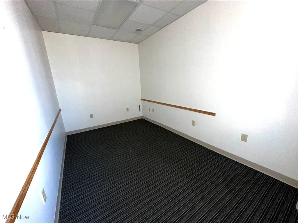 Unfurnished room featuring a drop ceiling and dark colored carpet