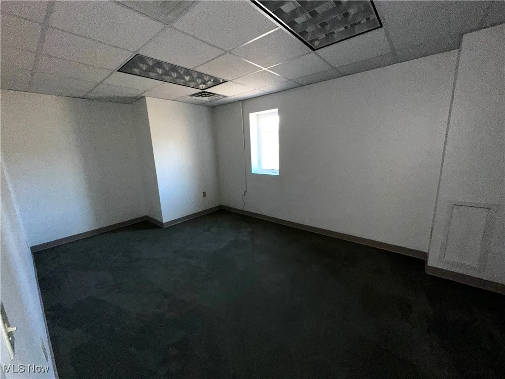 Spare room featuring dark carpet and a paneled ceiling