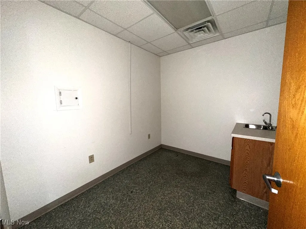 Empty room with a paneled ceiling, sink, and dark colored carpet