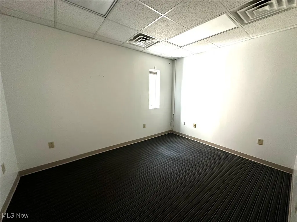 Empty room featuring a drop ceiling and dark carpet