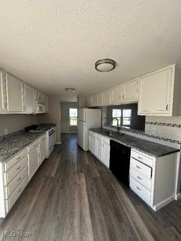 Kitchen featuring a textured ceiling, dark hardwood / wood-style flooring, white appliances, and white cabinets