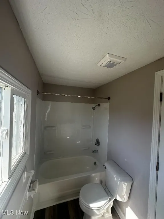 Bathroom featuring shower / bathing tub combination, hardwood / wood-style flooring, toilet, and a textured ceiling