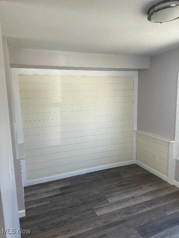 Empty room featuring a textured ceiling and dark hardwood / wood-style flooring