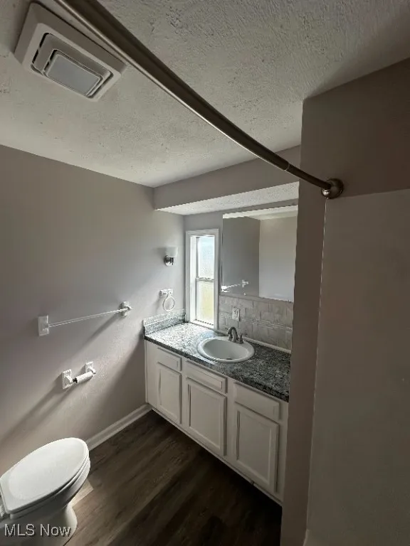 Bathroom featuring vanity, toilet, a textured ceiling, hardwood / wood-style floors, and decorative backsplash