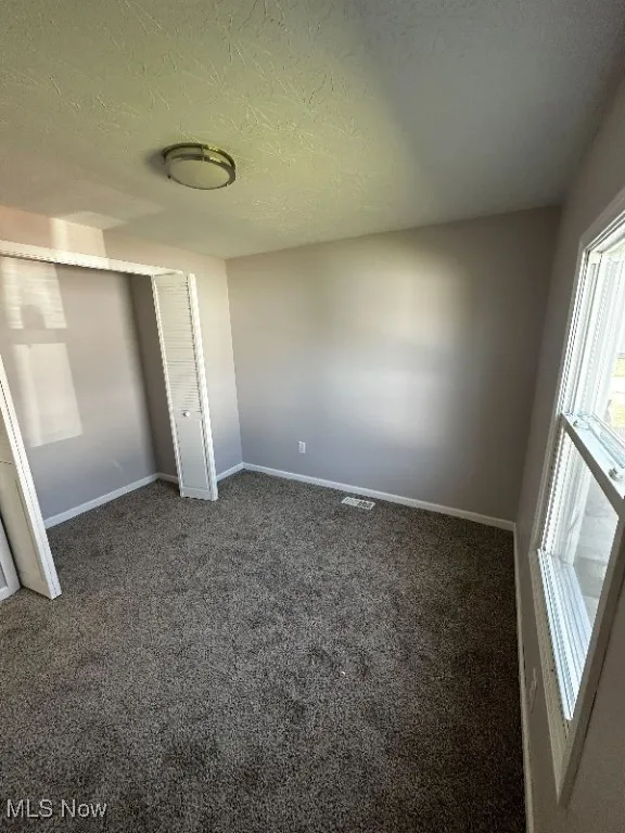 Unfurnished bedroom with dark carpet, a textured ceiling, and a closet