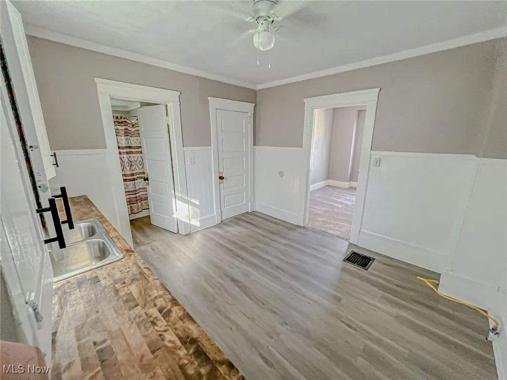 Unfurnished bedroom featuring light hardwood / wood-style floors, ornamental molding, sink, and ceiling fan
