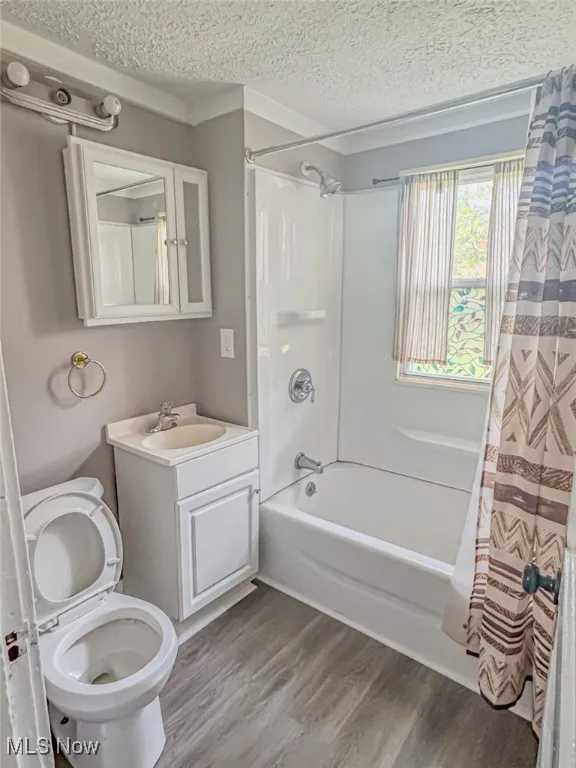 Full bathroom with shower / bath combination with curtain, a textured ceiling, wood-type flooring, toilet, and vanity