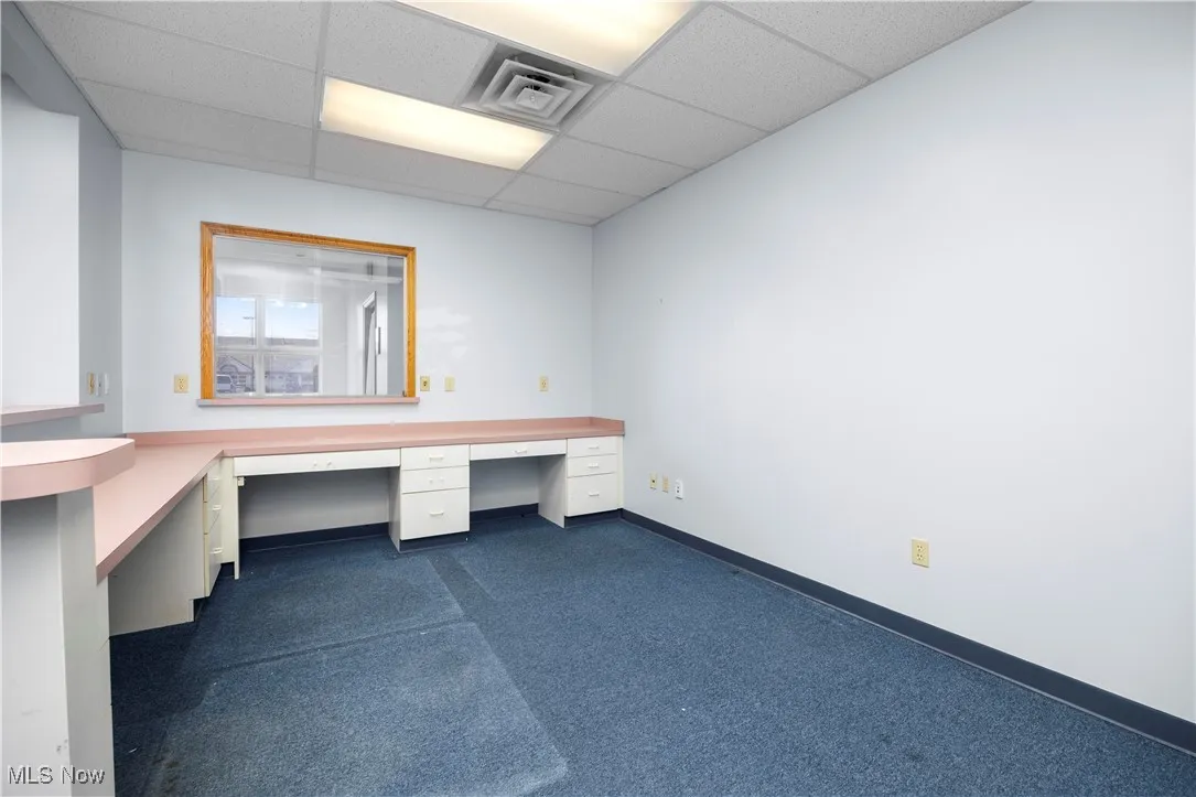Unfurnished office with a paneled ceiling, built in desk, and dark carpet