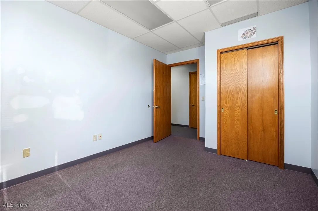 Unfurnished bedroom featuring a paneled ceiling, dark carpet, and a closet