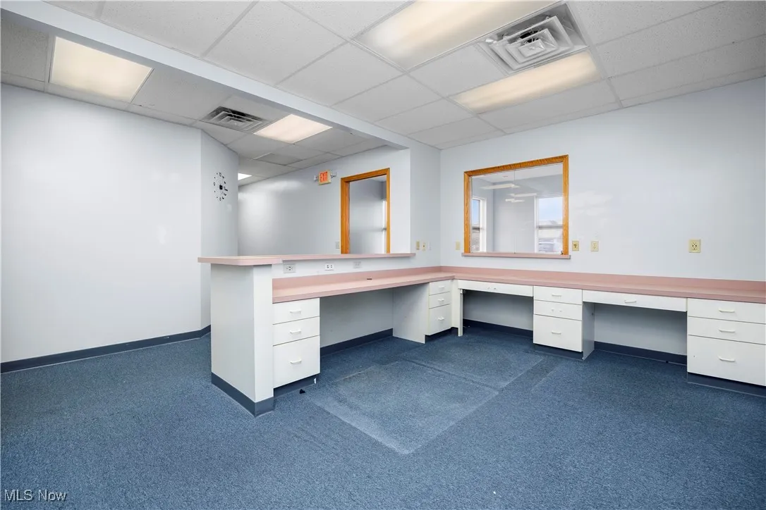 Unfurnished office featuring built in desk, dark colored carpet, and a drop ceiling