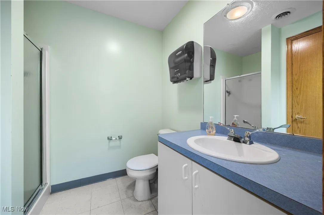 Bathroom with toilet, an enclosed shower, vanity, and tile patterned floors