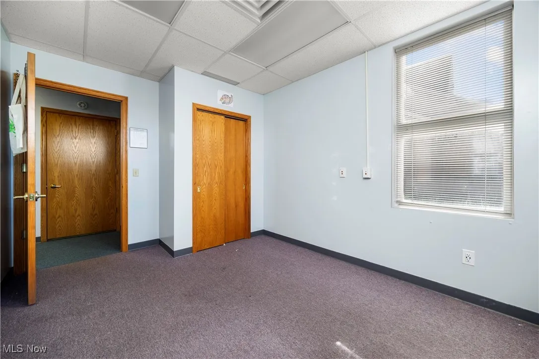 Unfurnished bedroom featuring a closet, dark carpet, and a drop ceiling