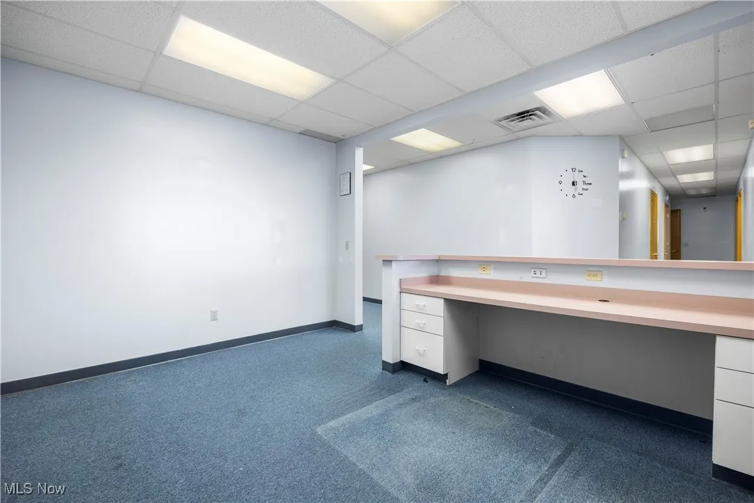 Unfurnished office featuring a drop ceiling, built in desk, and dark carpet