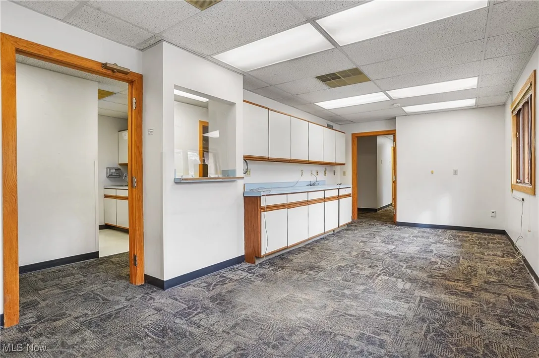 Kitchen with a drop ceiling, white cabinets, and dark colored carpet